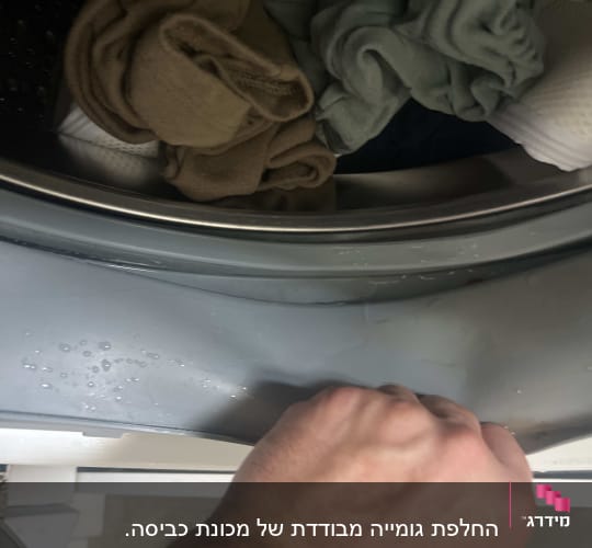 יד אוחזת בדלת מכונת כביסה עם בגדים בפנים